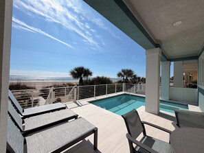 A poolside area with a view of the beach, lounge chairs, and a small pool.