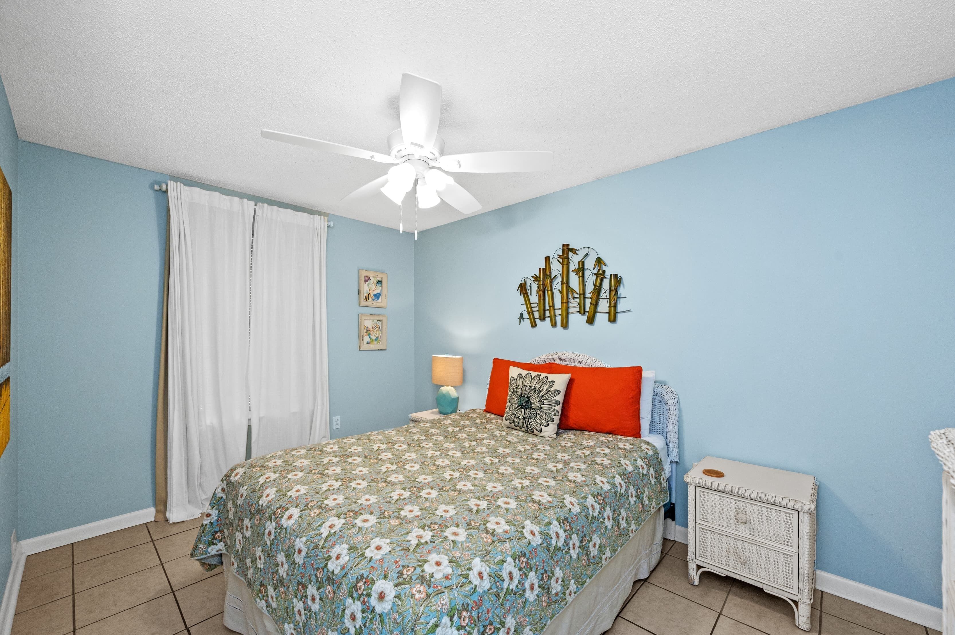 A bedroom with a bed, a ceiling fan, a nightstand, a lamp, and a wall decoration.
