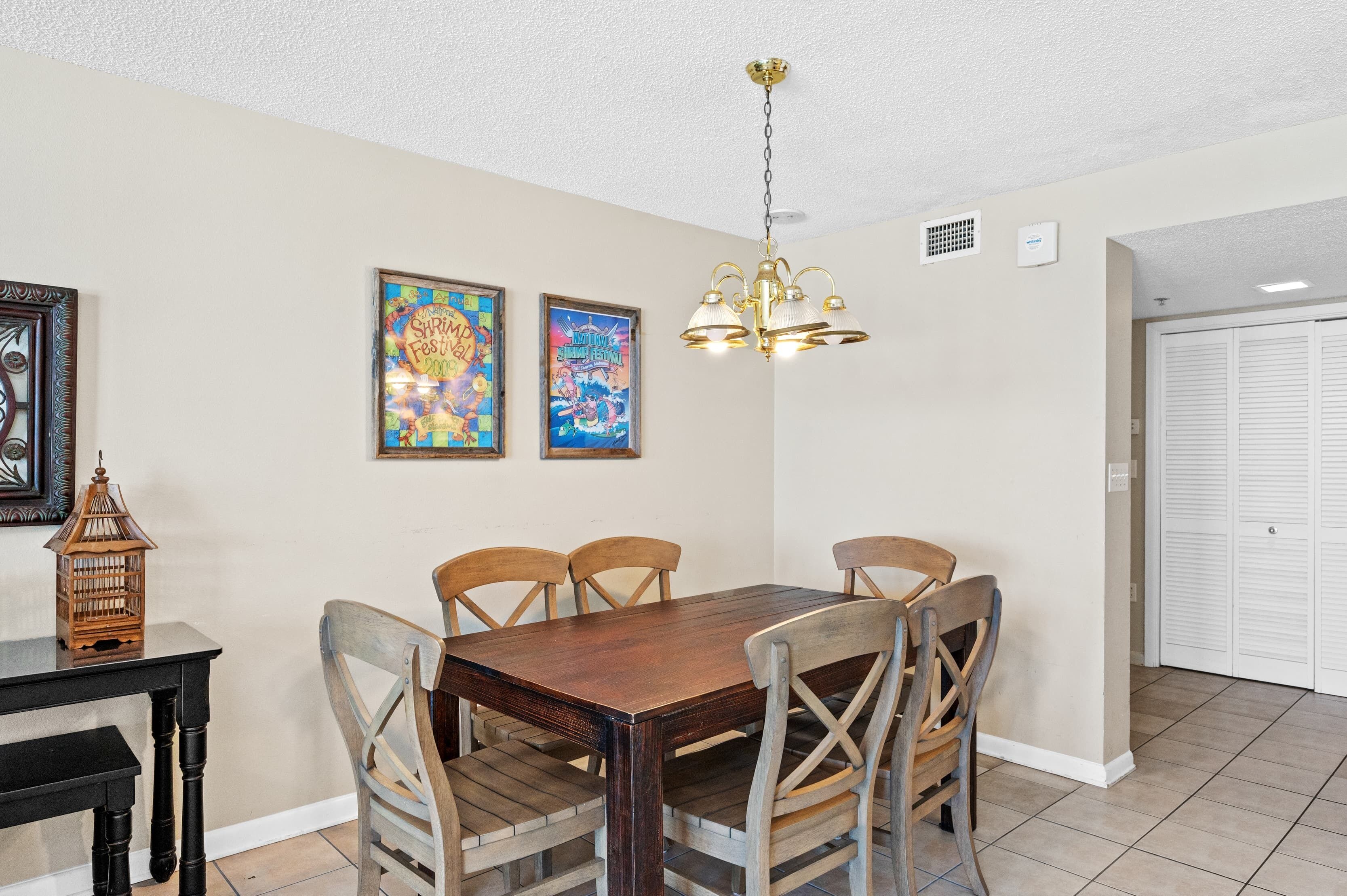 Un coin repas avec une table et des chaises en bois, un lustre et deux affiches encadrées au mur.