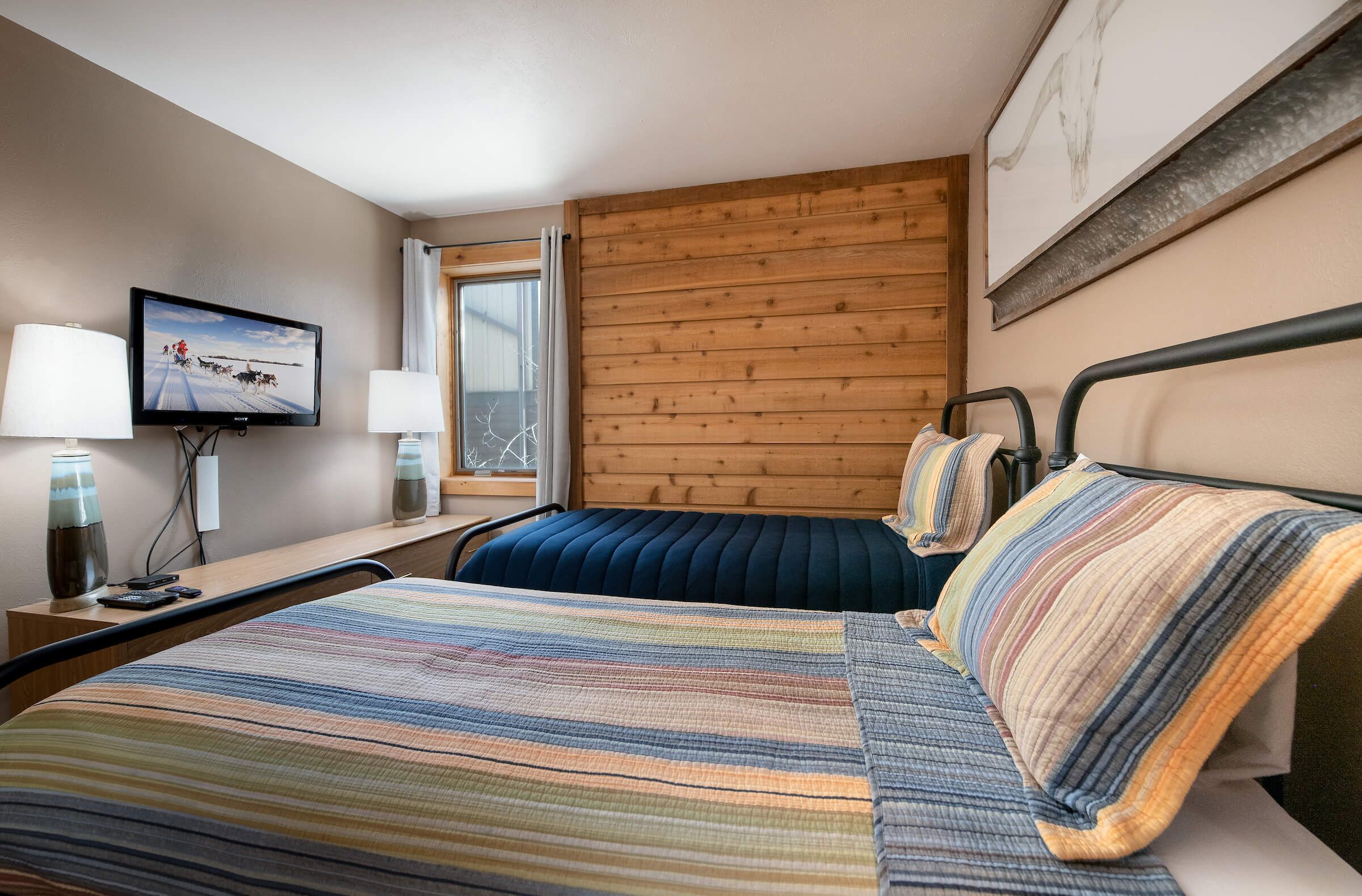 Una camera d'albergo con un letto, una televisione, una finestra e pannelli di legno sulla parete.