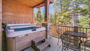 Een houten terras met een jacuzzi, buitenmeubels en een stenen muur.