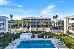 Un hôtel doté d’une piscine, de palmiers et surplombant un ciel bleu azur.
