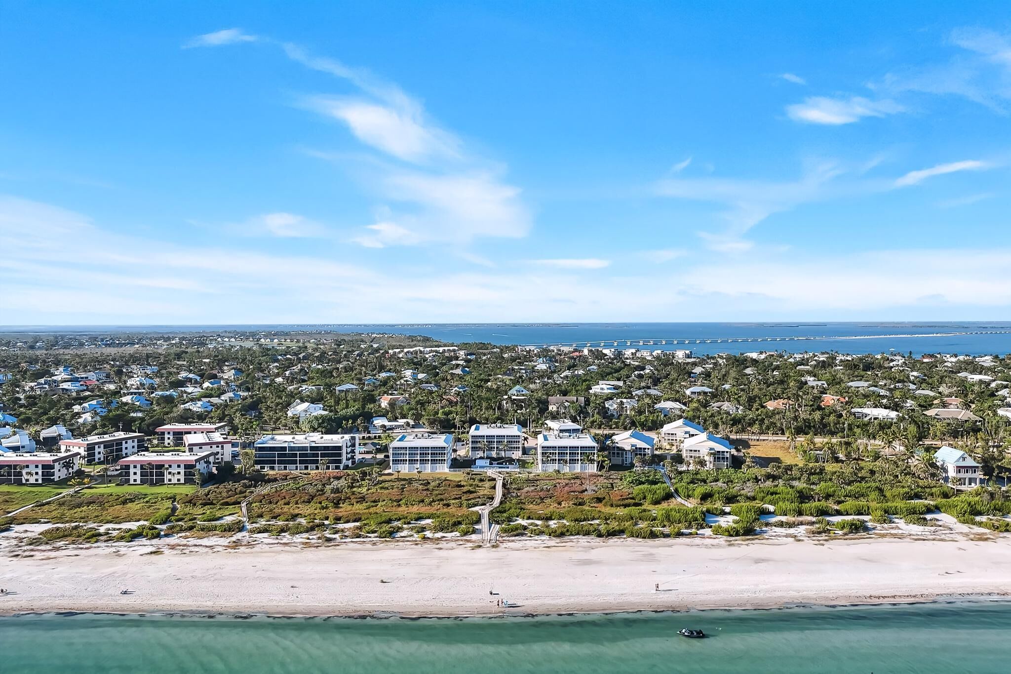 Un quartier résidentiel situé sur la côte, avec des propriétés donnant sur la plage, un ciel dégagé et une vue lointaine sur l’océan.
