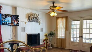 A room with a bed, a television, a fireplace, a ceiling fan, and a door with glass panels.