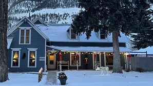 A two-story building with a porch, a Christmas tree, and a snow-covered landscape in the background.