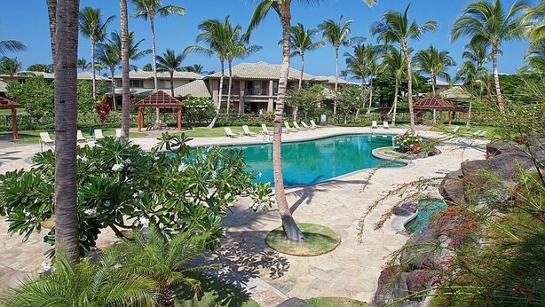 Een resort met een zwembad, omringd door palmbomen en ligbedden.