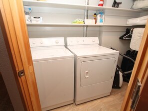 A laundry area with two white washing machines, a shelf with toiletries, and a hanging rack with a towel. - The Dogwood, Dog Friendly. Ski in/out, Hot tub (Mt. Crested Butte)