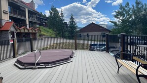 Un terrazzo in legno con una vasca idromassaggio, panchine e un'area recintata, sullo sfondo un'auto e degli edifici.