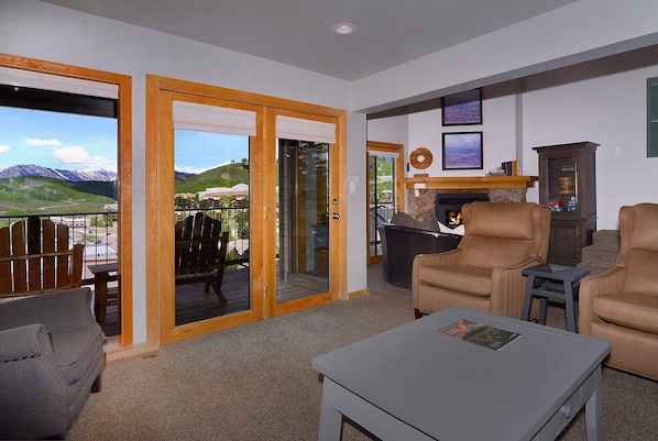 Un salon avec vue sur les montagnes, une cheminée et un balcon aménagé avec du mobilier d’extérieur.