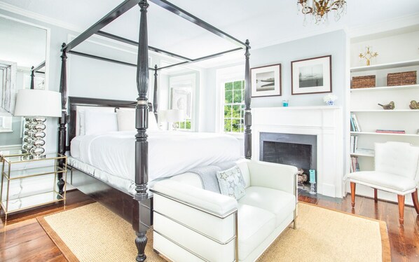 Una cama con dosel y cuatro columnas, un sofá blanco, un sillón blanco y una chimenea.