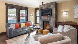 A living room with a fireplace, a sofa, a coffee table, and a TV mounted on the wall.