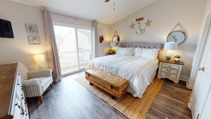 Un dormitorio con una cama grande, un banco de madera, una silla, un televisor y un balcón con cortinas.