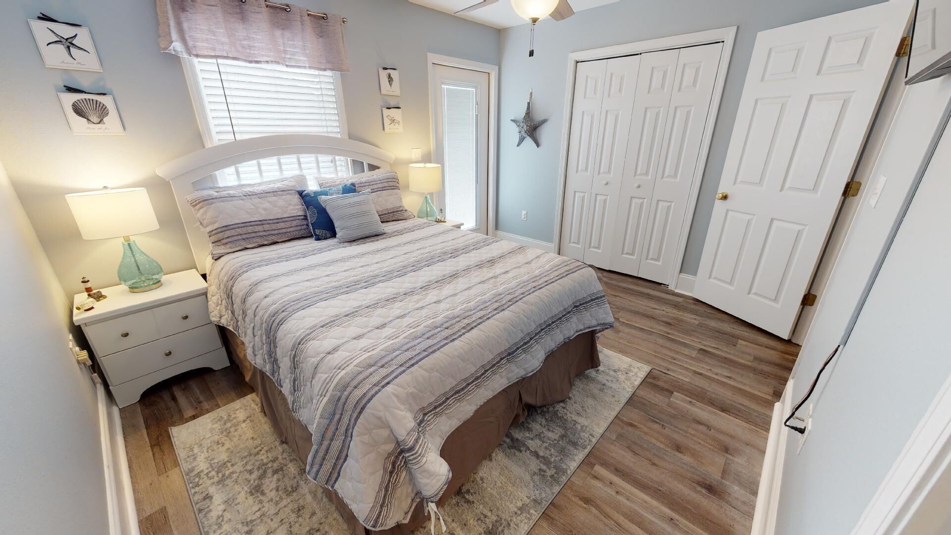 Une chambre à coucher avec un lit, des tables de chevet, une fenêtre avec des stores, une décoration en forme d’étoile et des portes blanches.