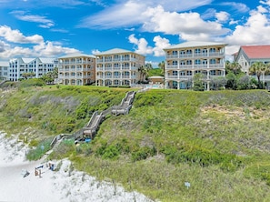 A beachfront hotel with multiple buildings, a staircase leading to the beach, and a sandy shoreline. - 30A Monterey B201 - Gulf Front Condo Near Alys Beach (Seacrest Beach)