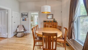 Une salle à manger avec une table et des chaises en bois, un luminaire suspendu et une fenêtre avec des rideaux.