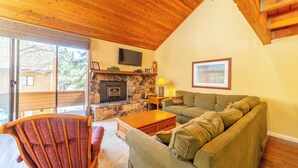 A cozy living room with a stone fireplace, wooden ceiling, and a large window.