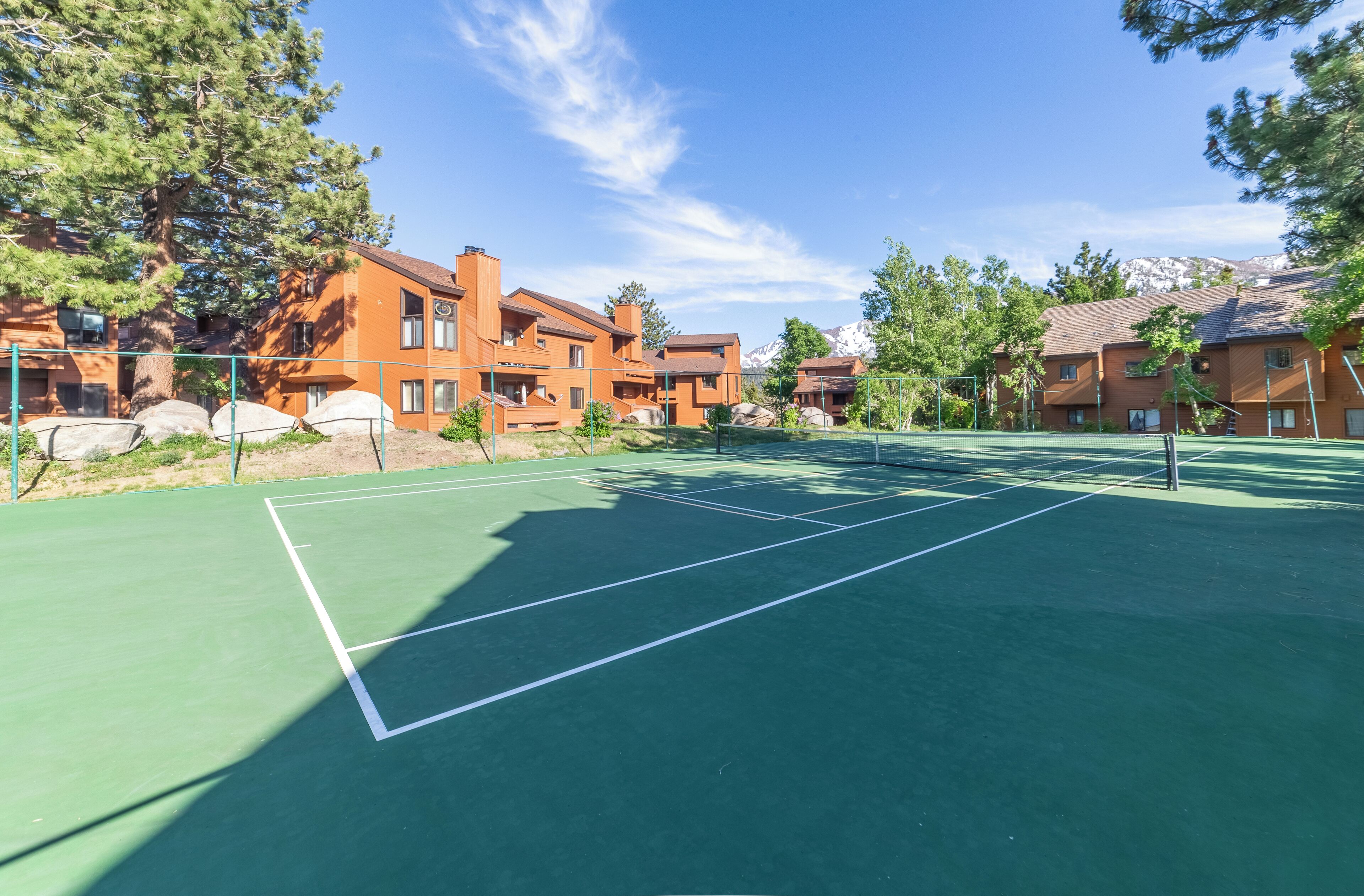 Un court de tennis doté d’une surface verte, entouré de bâtiments aux façades en briques et aux grandes fenêtres.
