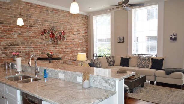 A kitchen with a granite countertop, a brick wall, and a dining area with a sofa and a coffee table.
