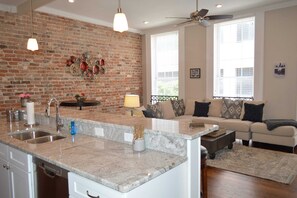 A kitchen with a granite countertop, a brick wall, and a dining area with a sofa and a coffee table. - Business / Industry Themed-The Picayune Newly renovated Historic Property (New Orleans)