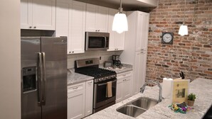 A kitchen with white cabinets, stainless steel appliances, a brick wall, and pendant lights.