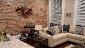 A living room with a brick wall, a beige sofa, a coffee table, and a patterned rug.