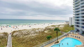 A beach view with a swimming pool, beach umbrellas, and a high-rise building. - Lighthouse 410 by Liquid Life (Gulf Shores)