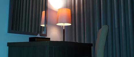 A hotel room with a desk, chair, lamp, and a large window with curtains.