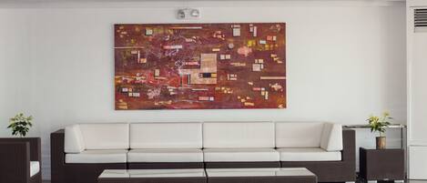 A modern living room with a white sofa, a brown ottoman, and a large abstract painting on the wall.