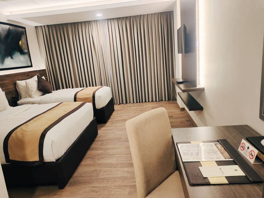 A hotel room with two beds, a TV, a desk with a chair, and a window with curtains.