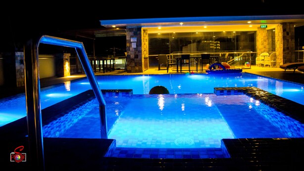 Una piscina con cerramiento de vidrio, un espacio de descanso con sillas y una señal de salida visible.