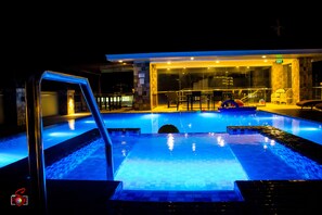 A swimming pool with a glass enclosure, a seating area with chairs, and a visible exit sign. - Hotel Marciano (Calamba)