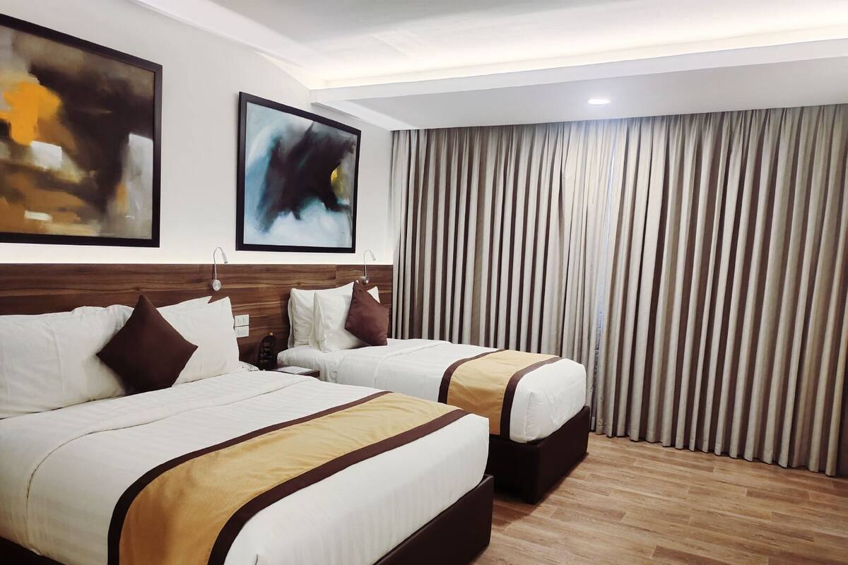 Habitación de hotel con dos camas, cabecera de madera, un cuadro abstracto grande y vista de una cortina.