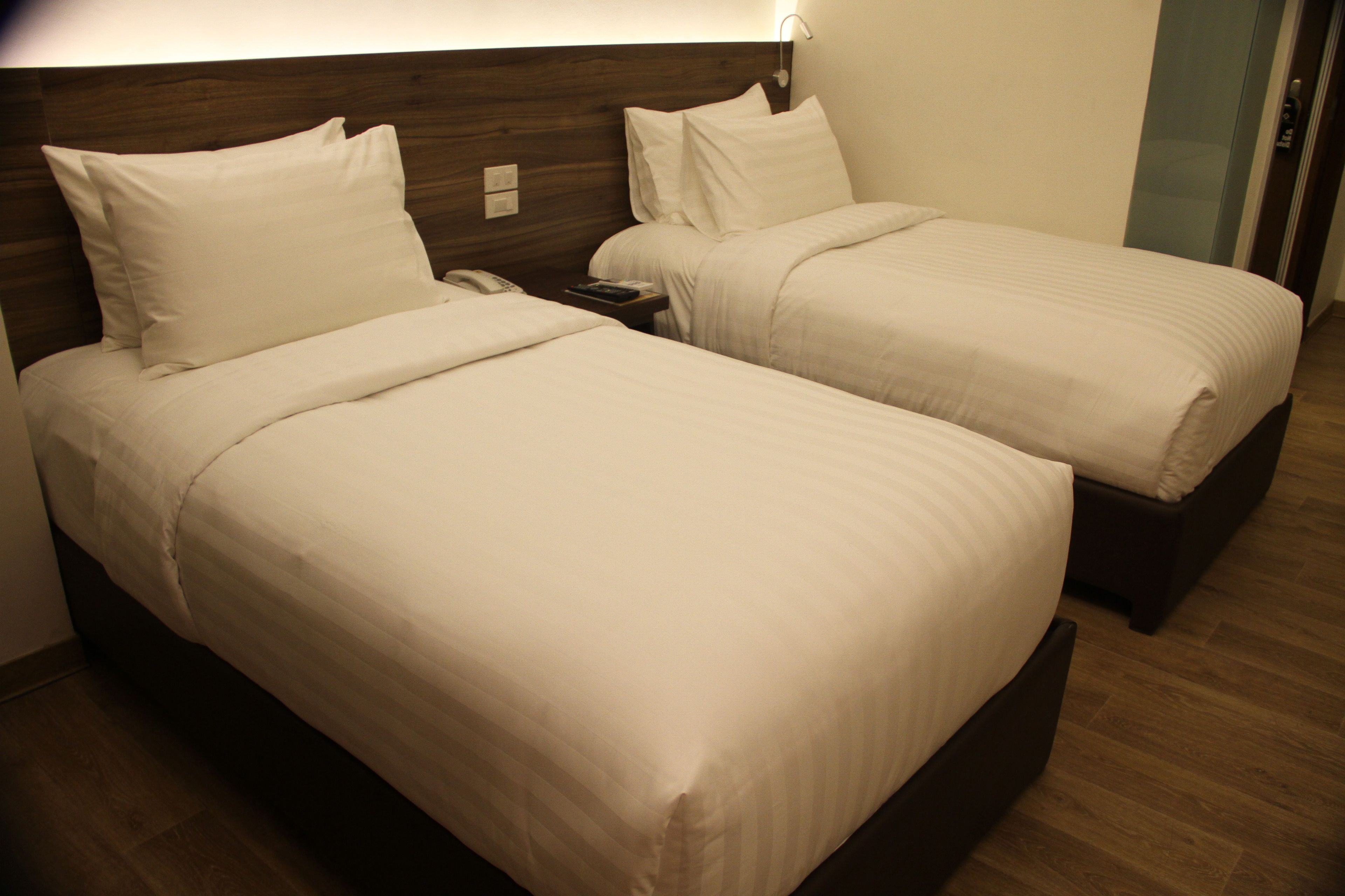 A hotel room with two single beds, a nightstand with a phone, and a wooden headboard.