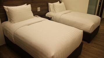A hotel room with two single beds, a nightstand with a phone, and a wooden headboard.