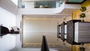 Un vestíbulo de hotel moderno con suelo de vidrio, una recepción y una zona de estar con vista al piso superior.
