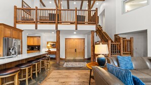 Amplio espacio tipo loft con techo alto, vigas de madera, cocina con barra y una zona de estar acogedora con un sofá de cuero y una lámpara.