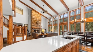Una cocina amplia con una isla grande, vigas de madera, chimenea de piedra y ventanas amplias que ofrecen vistas al exterior.
