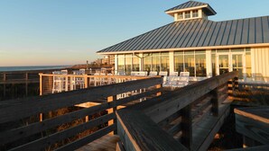 Un edificio frente a la playa con un muelle de madera y zona de estar al aire libre.