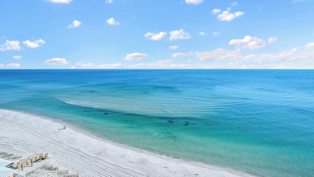 Une plage à l’eau turquoise et limpide, avec une promenade en bois qui mène au rivage.