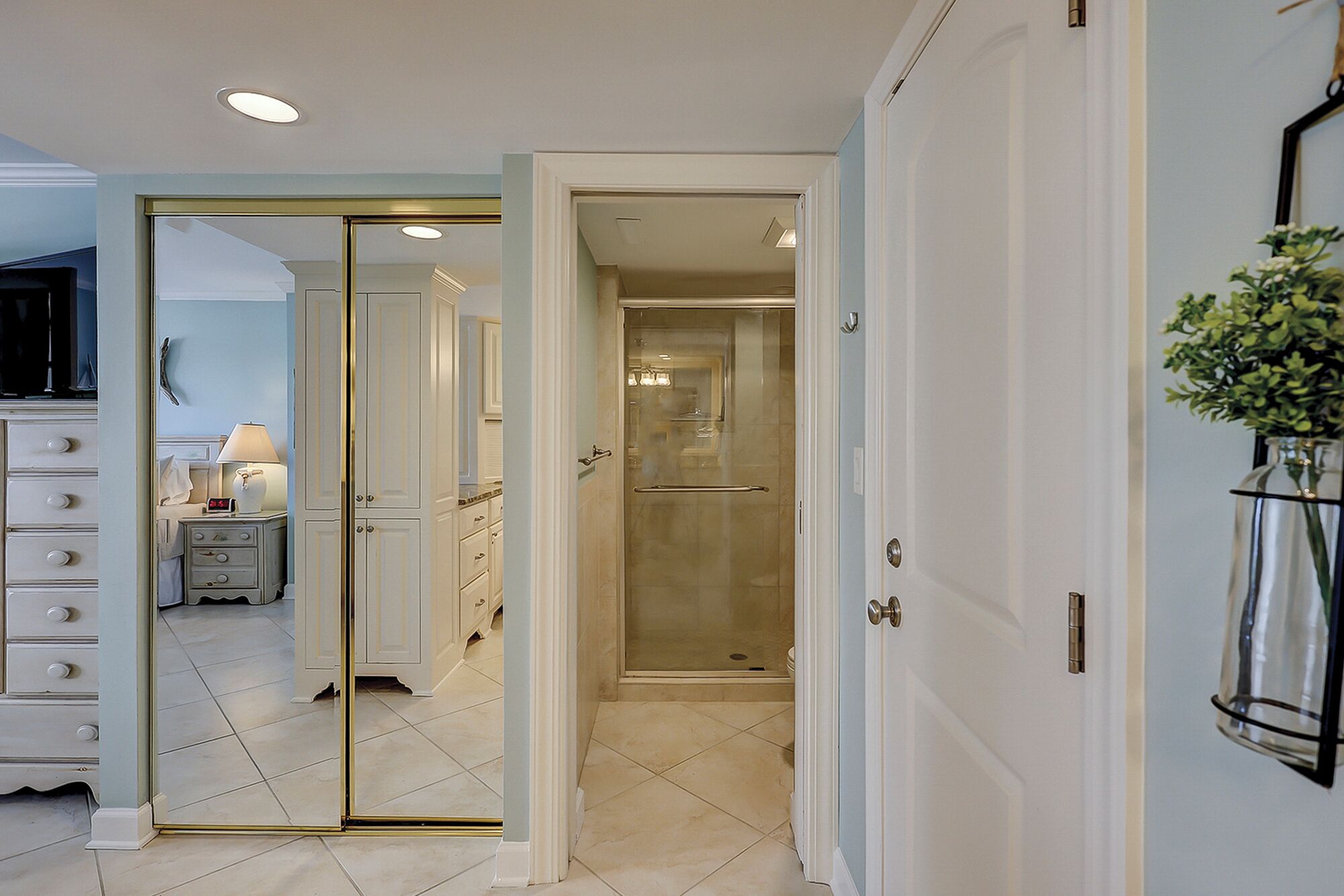 A hotel room with a large mirror, a vanity with drawers, a small table with a lamp, and a shower area.