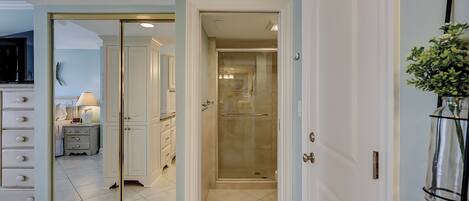 A hotel room with a large mirror, a vanity with drawers, a small table with a lamp, and a shower area.