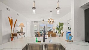 A modern kitchen with a large island, stainless steel sink, and pendant lighting. - Ocean View Escape | Balcony Views + Boardwalk to the Beach (Port Aransas)