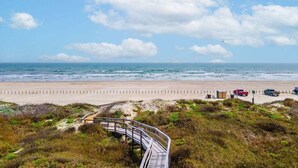 A beach with a wooden boardwalk leading to the shore, a sandy beach, and a clear sky. - Ocean View Escape | Balcony Views + Boardwalk to the Beach (Port Aransas)
