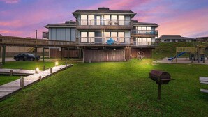 A multi-story building with a flat roof, a balcony on the second floor, and a playground in the background. - Ocean View Escape | Balcony Views + Boardwalk to the Beach (Port Aransas)
