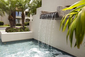 Una fontana con acqua a cascata, palme e una piscina con mosaici.