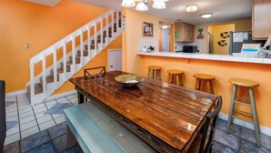 A dining area with a wooden table, bench, and stools. A staircase with white railings leads to another level. - 19 GulfBreeze Court👙Destin, FL🐟Pet Friendly🐶 (Destin)