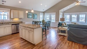 A spacious kitchen with wooden flooring, white cabinetry, and a dining area with chairs and a table.