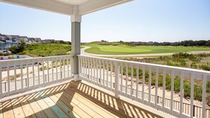A wooden deck with white railings overlooking a golf course and residential area.