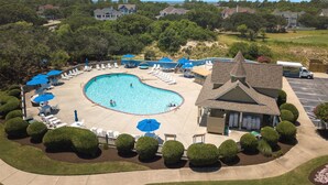 A swimming pool with lounge chairs and umbrellas, surrounded by well-maintained bushes and a building with a pitched roof.