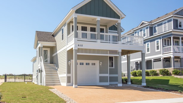 A two-story residential building with a covered front porch, a garage, and a well-maintained lawn.